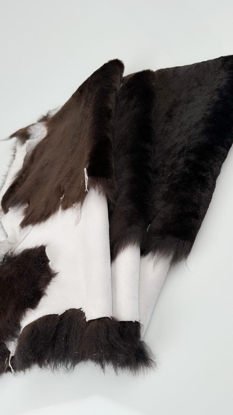 May include: A brown and white sheepskin rug with a soft, fluffy texture. The rug is folded in half, revealing the white underside.