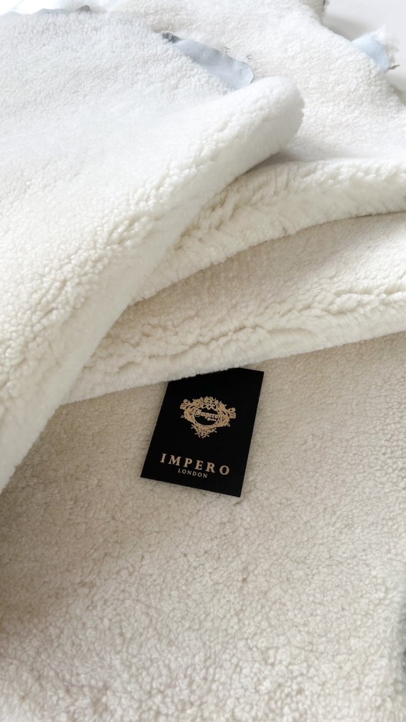 May include: A close-up of a white faux fur throw blanket with a black label that reads "Impero London".