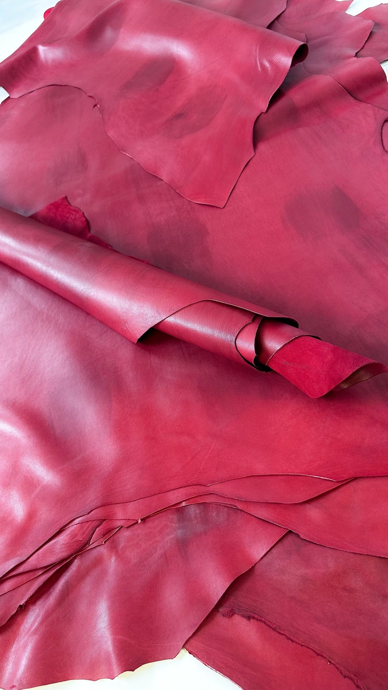 Pu&ograve; includere: Un mucchio di pelli di cuoio rosso, alcune arrotolate, che mostrano la trama e il colore del cuoio.