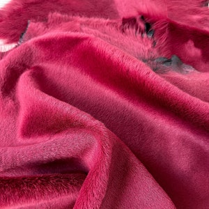 May include: A close-up of a deep red cowhide rug with a soft, fuzzy texture. The hide is folded and draped, showcasing the natural grain and colour variations.