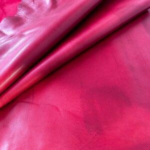 Pu&ograve; includere: Primo piano di un pezzo di pelle rosa scuro. La pelle &egrave; piegata a met&agrave;, mostrando la sua texture liscia e morbida.