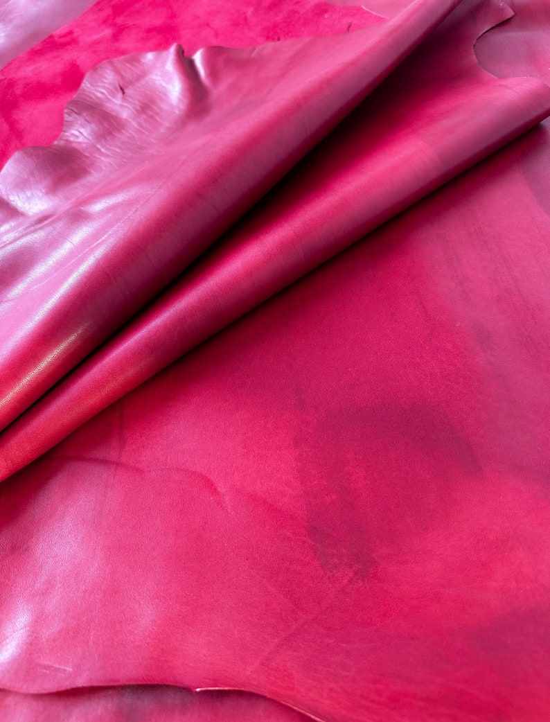 Pu&ograve; includere: Primo piano di un pezzo di pelle rosa scuro. La pelle &egrave; piegata a met&agrave;, mostrando la sua texture liscia e morbida.
