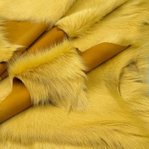 May include: Close-up of a piece of yellow fur with a soft, textured appearance. The fur is layered, revealing a tan leather backing. The overall colour is a vibrant, sunny yellow.