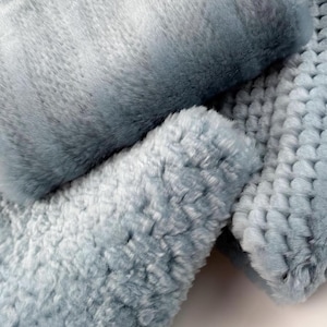 May include: Two soft, plush, light blue faux fur throw pillows. The pillows are made of a fluffy, textured fabric.