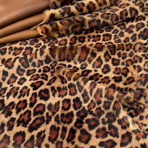May include: A brown and black faux fur fabric with a leopard print pattern.