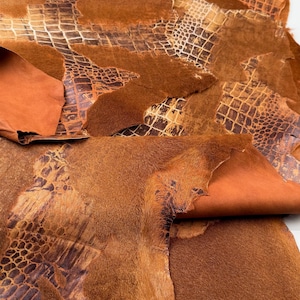 May include: A collection of brown leather hides with different textures, including a crocodile pattern. The hides are stacked on top of each other and have a rustic, vintage look.