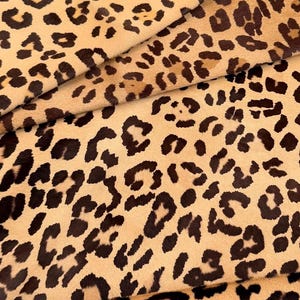 May include: Close-up of a tan and brown leopard print fabric. The fabric is folded in layers, showing the pattern from different angles.