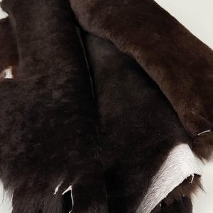 May include: A pile of brown sheepskin hides with the fur side facing up. The hides are folded and layered on top of each other.