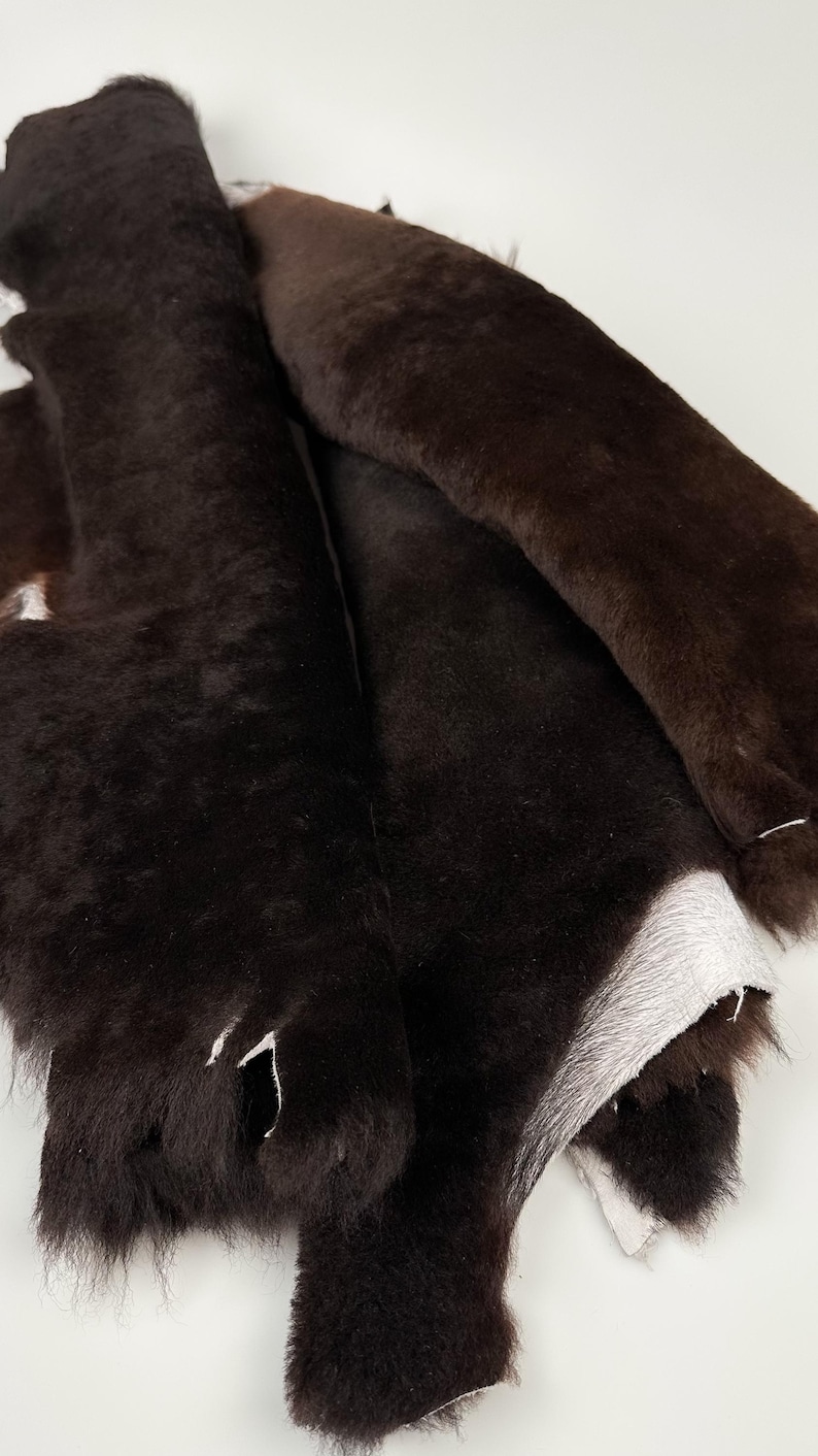 May include: A pile of brown sheepskin hides with the fur side facing up. The hides are folded and layered on top of each other.