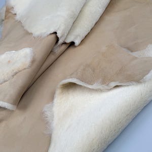 K&ouml;nnte beinhalten: Ein beiger Schaffellteppich mit einer wei&szlig;en Fellseite. Der Teppich ist in der Mitte gefaltet und zeigt beide Seiten.