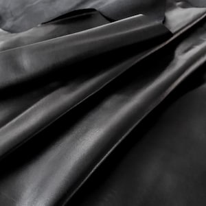 May include: A close-up of black leather, folded and draped, showing the texture and grain of the material.