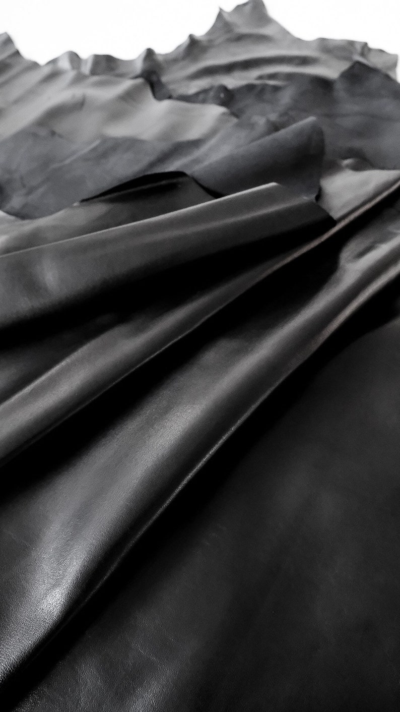 May include: A close-up of black leather, folded and draped, showing the texture and grain of the material.