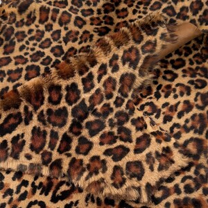 May include: Close-up of a brown and black leopard print faux fur fabric. The fabric has a soft, plush texture and is ideal for crafting projects.