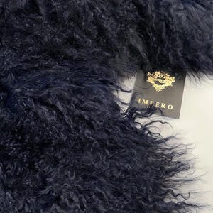 May include: A close-up of a dark blue fluffy fur fabric. The fabric has a soft, curly texture. The fabric is labelled "Impero" in gold lettering.