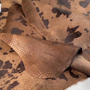 May include: A close-up of a brown snakeskin leather with a dark brown pattern. The leather is folded and textured.