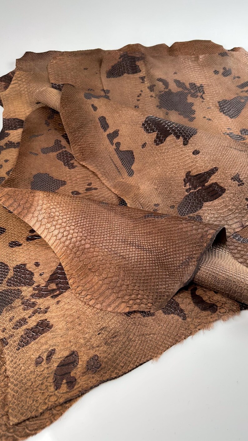 May include: A close-up of a brown snakeskin leather with a dark brown pattern. The leather is folded and textured.