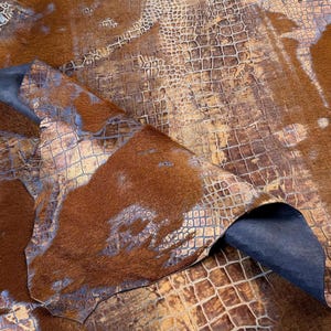 May include: A brown cowhide rug with a gold and brown crocodile pattern overlay. The rug has a soft, fuzzy texture.