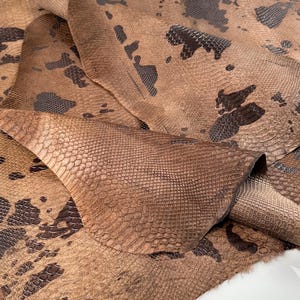 May include: A piece of brown snakeskin leather with a dark brown pattern. The leather is folded and textured.