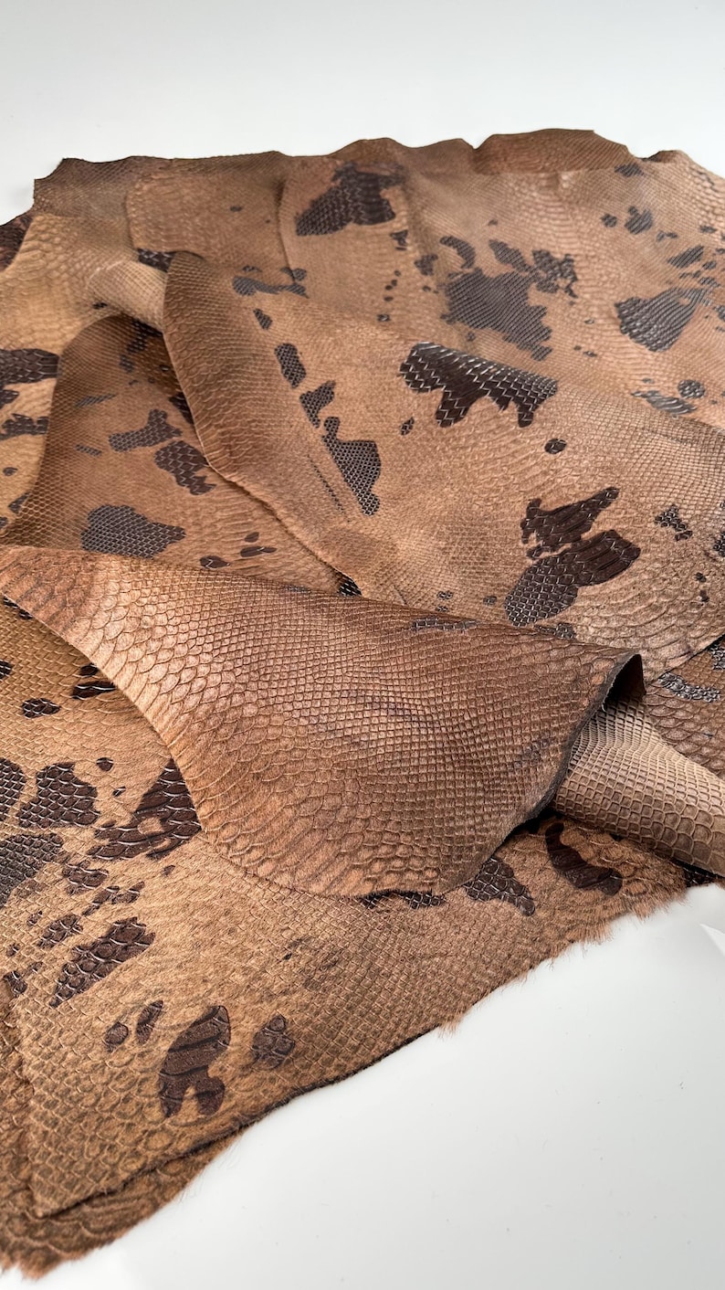 May include: A piece of brown snakeskin leather with a dark brown pattern. The leather is folded and textured.