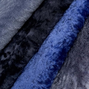 Op de afbeelding: Close-up van verschillende pluche stoffen in blauwtinten. De texturen variëren van glad tot harig, met kleuren variërend van lichtblauw tot diep marineblauw. De stoffen zijn diagonaal gerangschikt en tonen hun verschillende texturen en tinten.