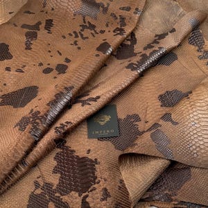 May include: Brown snakeskin leather with a dark brown pattern. The leather is folded and shows the texture of the skin. The leather has a label that says "Impero London".