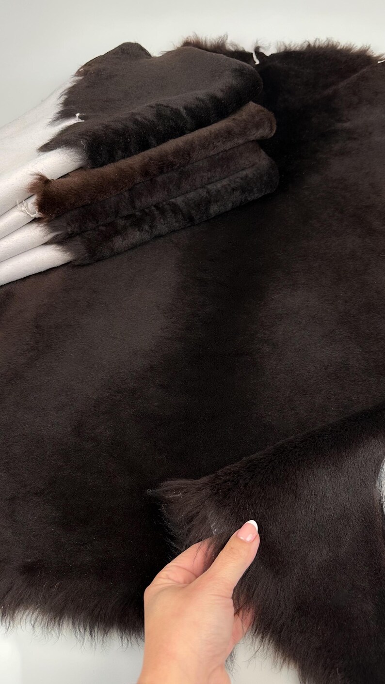 May include: A close-up of a dark brown faux fur fabric. The fabric is soft and fluffy, with a short pile. The fabric is folded in half, and the edges are frayed.