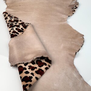 May include: A large piece of tan leather with a leopard print accent. The leopard print is brown and black spots on a tan background. The leather is folded over, revealing the leopard print.