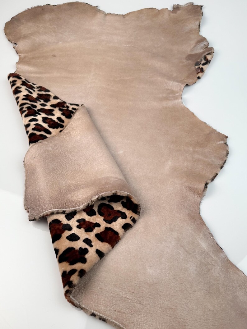 May include: A large piece of tan leather with a leopard print accent. The leopard print is brown and black spots on a tan background. The leather is folded over, revealing the leopard print.