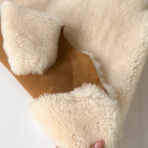 May include: A white sheepskin rug with a brown suede backing. The rug is folded in half and being held by a hand.
