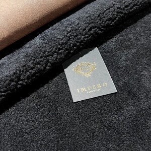 May include: Close-up of a black faux fur fabric with a brown suede fabric folded over it. A white tag with gold lettering reads "Impero London".