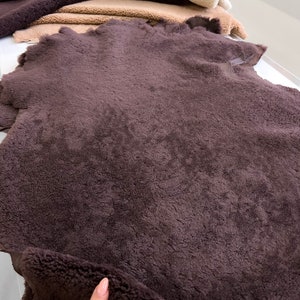 May include: Close-up of several pieces of faux fur fabric in various shades of brown and beige. The fabrics have a soft, textured appearance, with a deep, rich brown piece in the foreground.
