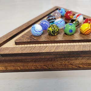 May include: A wooden marble game set featuring a triangular playing board and a collection of colorful glass marbles. The marbles display various patterns, including swirls, spots, and stripes, in shades of blue, green, yellow, and red.