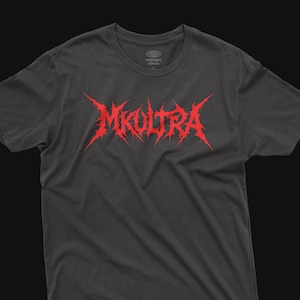 May include: A dark gray short-sleeved t-shirt featuring the text MKULTRA in a jagged, red, metal-style font across the chest. The inner neck label displays the text midnight climax with a globe icon and the size M printed below it.