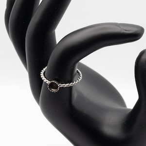 May include: A silver ring with a round, open bezel setting. The ring is on a black hand model.