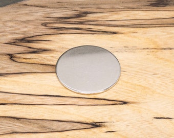 Puede incluir: Un disco redondo de metal plateado sobre una superficie de madera.