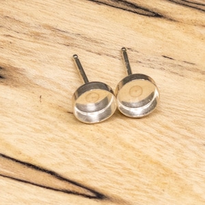 Puede incluir: Dos postes de pendientes de plata con biseles redondos y planos de plata. Los biseles están vacíos y listos para ser rellenados con un cabujón.