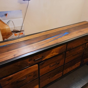 May include: A long wooden dresser with a black metal frame and blue resin inlay. The dresser has multiple drawers with black metal handles.