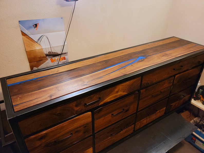 May include: A long wooden dresser with a black metal frame and blue resin inlay. The dresser has multiple drawers with black metal handles.