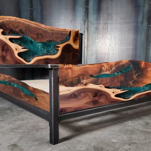 May include: A king-size bed frame made of dark wood with a natural edge and a teal blue epoxy resin inlay. The frame is supported by a black metal frame.