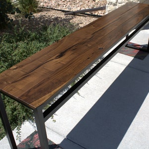 Op de afbeelding: Een lange, smalle consoletafel met een donkerhouten blad en een zwart metalen frame. De tafel is gemaakt van massief hout en heeft een rustieke, industriële uitstraling.