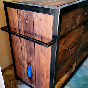 May include: A wooden dresser with a black metal frame and blue resin inlay. The dresser has multiple drawers with black metal handles.