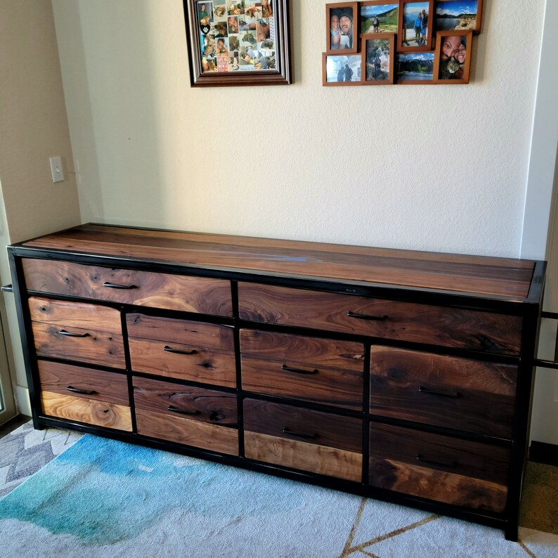 May include: A dark wood dresser with a black metal frame and nine drawers. The dresser has a smooth, polished finish and is made of high-quality materials.