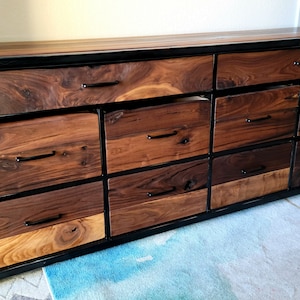 May include: A long, wooden dresser with a black metal frame and multiple drawers. The drawers are made of different types of wood, creating a unique and rustic look.