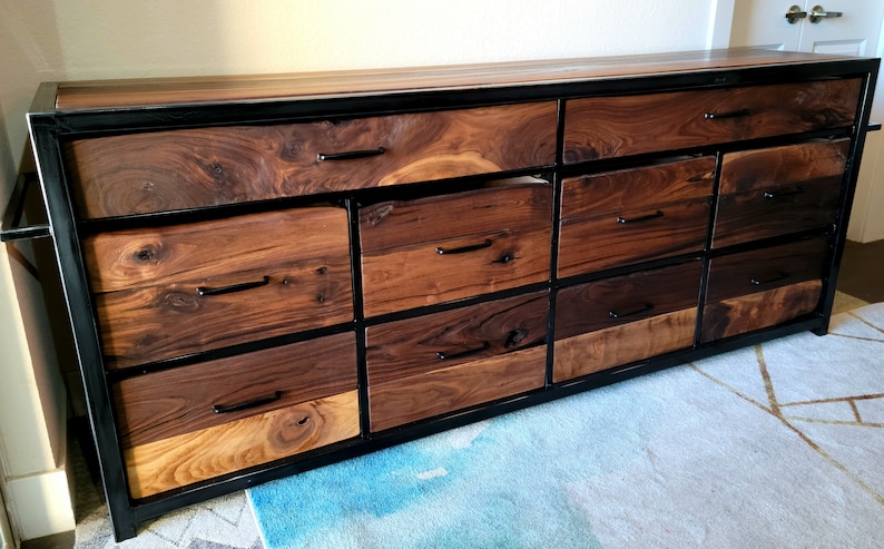 May include: A long, wooden dresser with a black metal frame and multiple drawers. The drawers are made of different types of wood, creating a unique and rustic look.