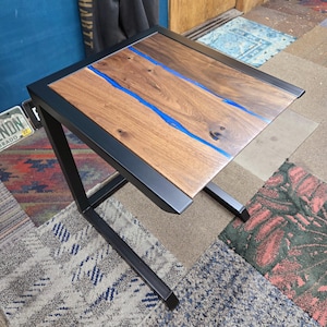 May include: A small, black metal side table with a wooden top. The top has a blue resin inlay that resembles a river.
