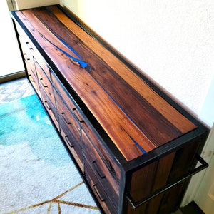 May include: A wooden dresser with a black metal frame and blue resin inlay. The dresser has multiple drawers and a long handle.