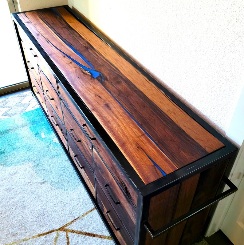 May include: A wooden dresser with a black metal frame and blue resin inlay. The dresser has multiple drawers and a long handle.