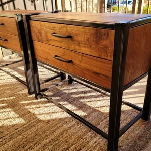 May include: Two wooden nightstands with black metal frames and two drawers each. The nightstands are sitting on a light brown rug.