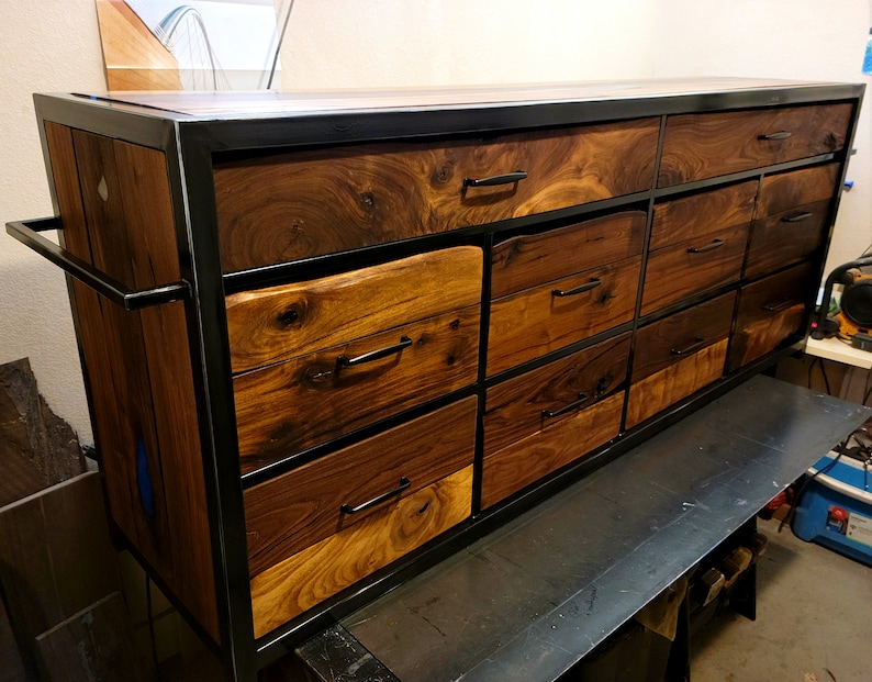 May include: A large dresser with a black metal frame and multiple drawers made of walnut wood. The drawers have black metal handles.