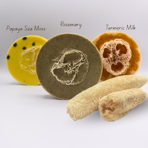 Może przedstawiać: Trzy okrągłe mydła z etykietami "Papaya Sea Moss", "Rosemary" i "Turmeric Milk" z naturalną luffą. Mydła są żółte, zielone i pomarańczowe. Dwie luffy są na pierwszym planie.